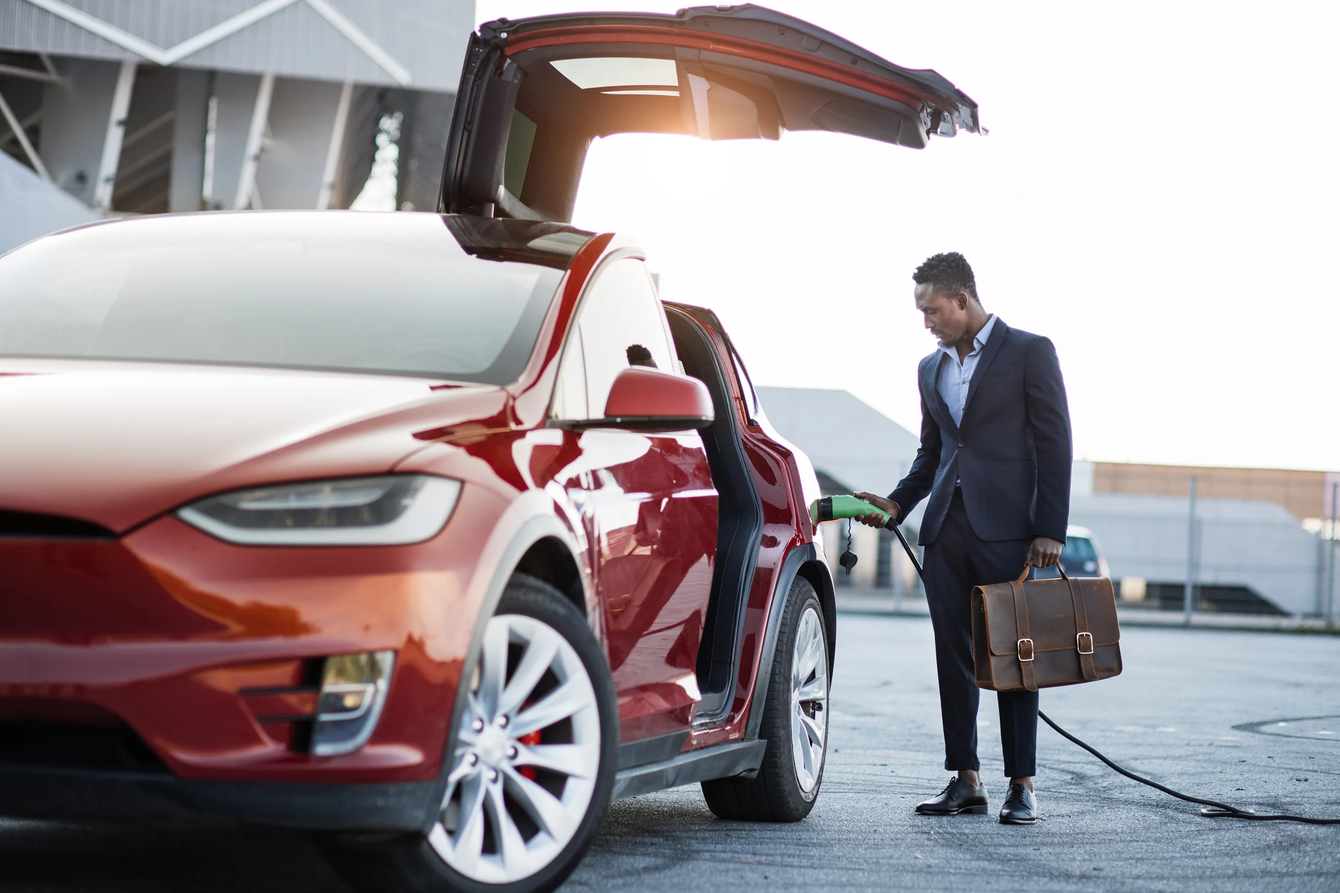 Business man with suitcase charging a red Tesla Model X.